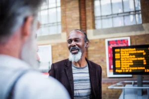 A man with a grey beard chats warmly at Leeds railway station, supporting others, community context, Doing Good Leeds.