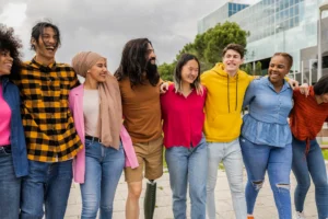 Seven young adults smiling together outside a modern building in Leeds, showing community spirit for Doing Good Leeds volunteering.