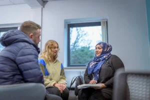 Three people in discussion as a woman in hijab speaks, volunteering meeting, bright room, Leeds, Doing Good Leeds.